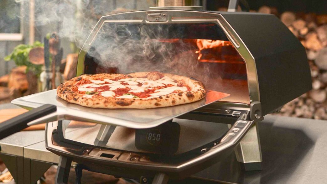 Pizza fresh from an Ooni Koda 16 outdoor pizza oven, captured mid-bake as a temperature reader checks the stone’s heat.