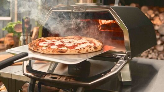 Pizza fresh from an Ooni Koda 16 outdoor pizza oven, captured mid-bake as a temperature reader checks the stone’s heat.