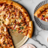 Close-up of a homemade BBQ chicken pizza topped with shredded chicken in tangy sauce, smoked gouda, mozzarella, red onion, and fresh cilantro.