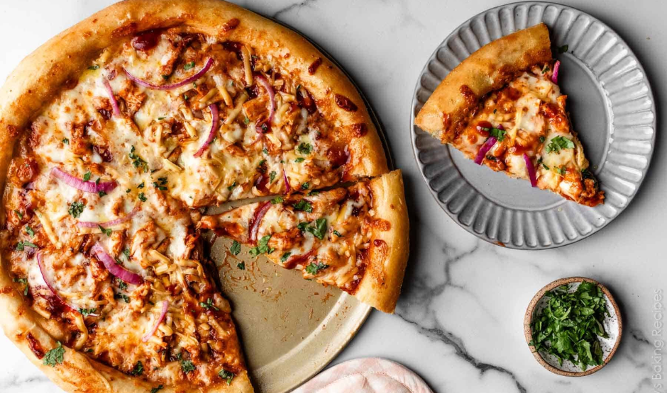 Close-up of a homemade BBQ chicken pizza topped with shredded chicken in tangy sauce, smoked gouda, mozzarella, red onion, and fresh cilantro.