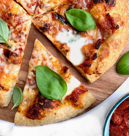 Home baker stretching pizza dough by hand in a kitchen, aiming for restaurant-quality crust.