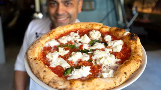 Chef demonstrating hand-stretching of Neapolitan pizza dough in a rustic kitchen setting.