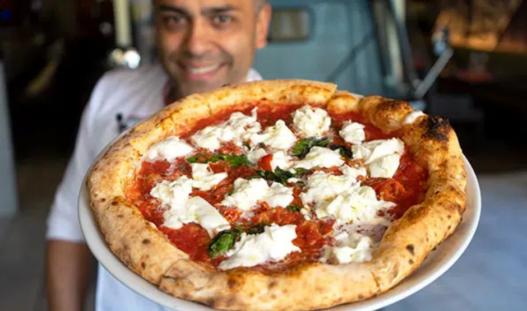 Chef demonstrating hand-stretching of Neapolitan pizza dough in a rustic kitchen setting.