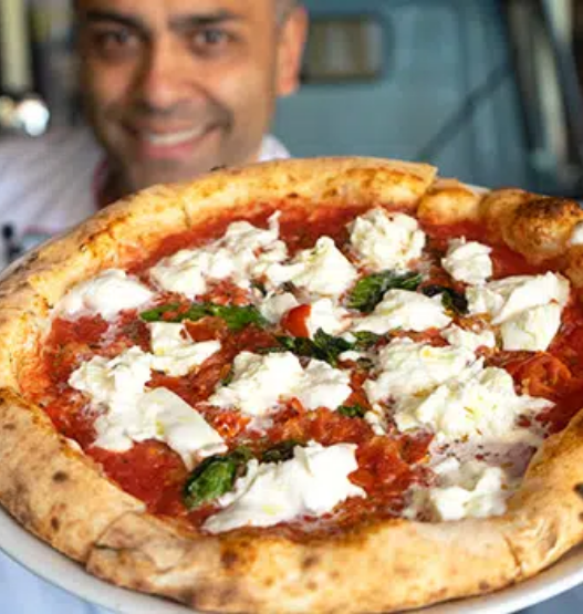 Chef demonstrating hand-stretching of Neapolitan pizza dough in a rustic kitchen setting.