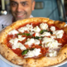 Chef demonstrating hand-stretching of Neapolitan pizza dough in a rustic kitchen setting.