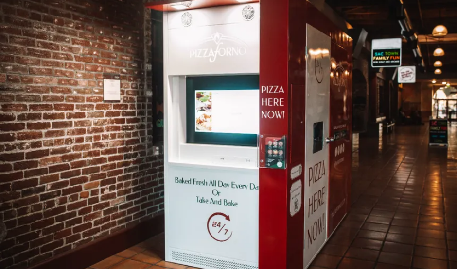 Red-and-white PizzaForno vending machine dispensing a freshly baked 12-inch pizza in California.