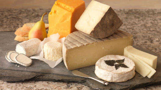 Wedge of soft-ripened cheese like Brie being cut, showing creamy interior under bloom rind.
