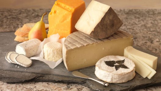 Wedge of soft-ripened cheese like Brie being cut, showing creamy interior under bloom rind.
