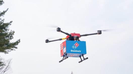 Domino’s drone in mid-air delivering pizza to a New Zealand couple, marking the world’s first commercial drone pizza delivery.