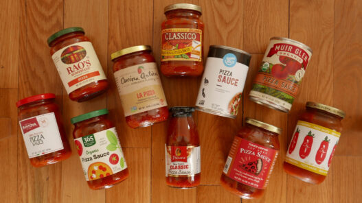 A display of eleven grocery-store pizza sauce jars and cans arranged on a wooden board.