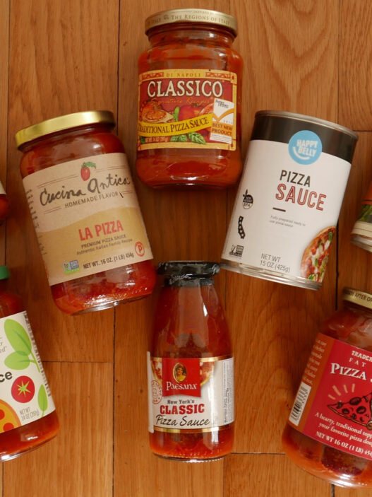 A display of eleven grocery-store pizza sauce jars and cans arranged on a wooden board.