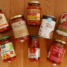 A display of eleven grocery-store pizza sauce jars and cans arranged on a wooden board.