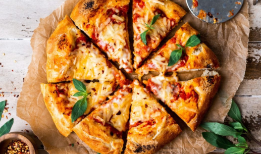 Sliced homemade vegan pizza topped with melty vegan cheese and fresh basil on a wooden board.