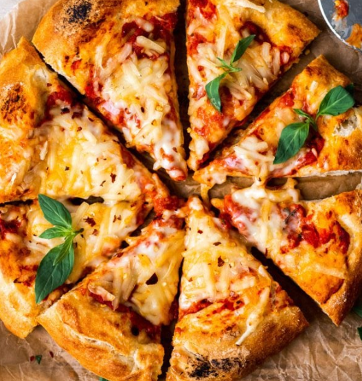 Sliced homemade vegan pizza topped with melty vegan cheese and fresh basil on a wooden board.