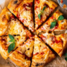 Sliced homemade vegan pizza topped with melty vegan cheese and fresh basil on a wooden board.