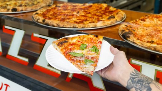 Thin-crust New York–style pizza slice from Outta Sight Pizza in San Francisco’s Chinatown, featuring melty cheese and charred edges.