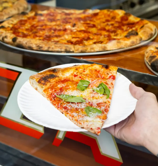 Thin-crust New York–style pizza slice from Outta Sight Pizza in San Francisco’s Chinatown, featuring melty cheese and charred edges.
