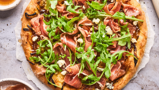 Freshly baked Fig & Prosciutto Pizza with mozzarella, arugula, and balsamic drizzle on a wooden board.