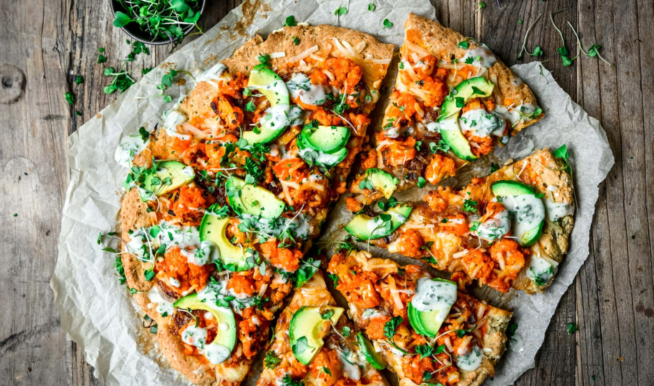 Hot and spicy Buffalo Cauliflower Vegan Pizza topped with vegan cheese, red onion, and ranch drizzle on a crispy crust
