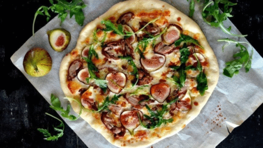 Duck Confit & Fig Pizza topped with goat cheese, arugula, and balsamic glaze on a rustic wooden board – Downtown LA gourmet style.