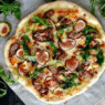 Duck Confit & Fig Pizza topped with goat cheese, arugula, and balsamic glaze on a rustic wooden board – Downtown LA gourmet style.