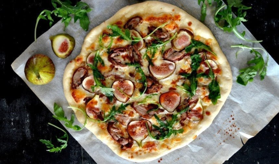 Duck Confit & Fig Pizza topped with goat cheese, arugula, and balsamic glaze on a rustic wooden board – Downtown LA gourmet style.