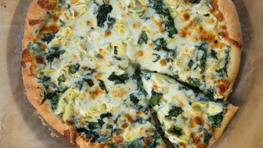 Grilled artichoke and spinach pizza with feta and mozzarella on a golden crust, served on a wooden board – inspired by Venice Beach flavors.