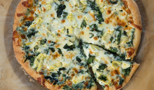 Grilled artichoke and spinach pizza with feta and mozzarella on a golden crust, served on a wooden board – inspired by Venice Beach flavors.