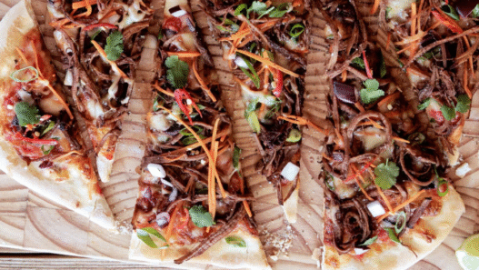 Korean BBQ beef pizza topped with bulgogi, kimchi, scallions, and gochujang aioli on a crispy crust
