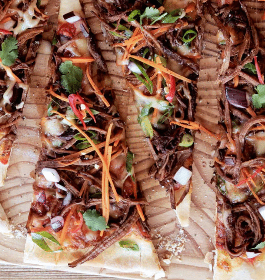 Korean BBQ beef pizza topped with bulgogi, kimchi, scallions, and gochujang aioli on a crispy crust
