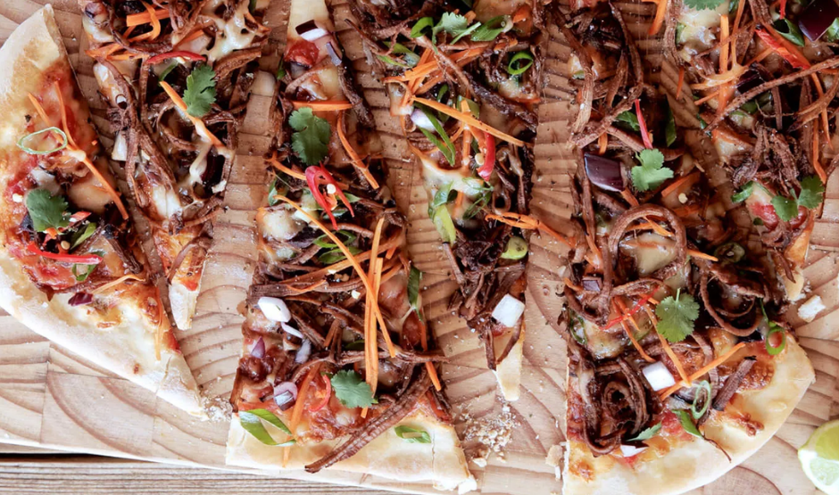 Korean BBQ beef pizza topped with bulgogi, kimchi, scallions, and gochujang aioli on a crispy crust