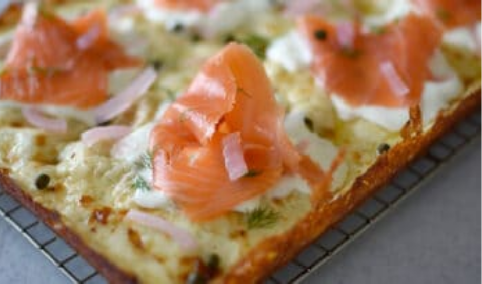 Top-down view of Lox and Cream Cheese Pizza topped with smoked salmon, red onions, capers, and arugula on a golden crust – LA brunch-inspired.