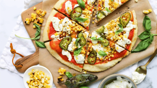 Roasted corn and jalapeño pizza on a wooden board with melted cheese and cilantro