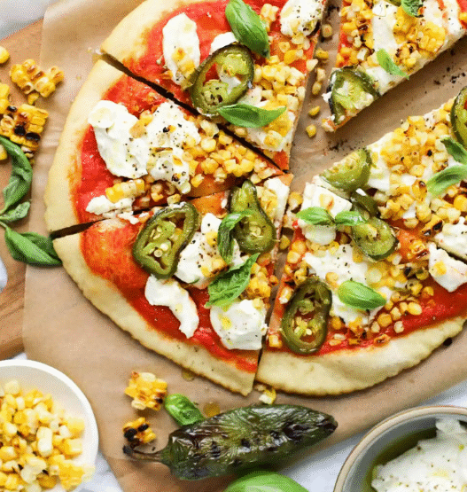 Roasted corn and jalapeño pizza on a wooden board with melted cheese and cilantro