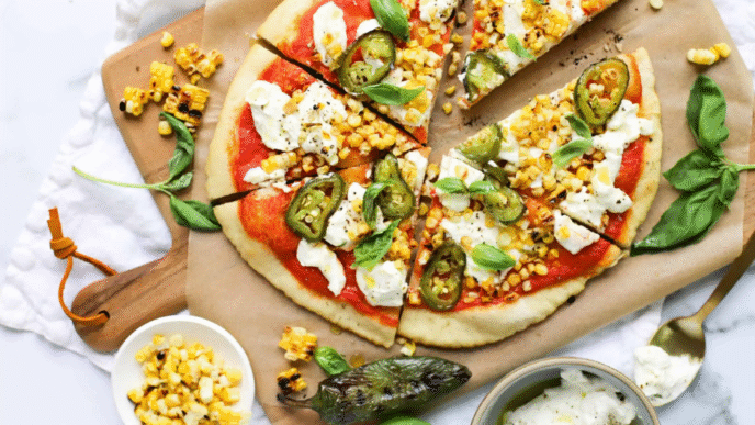 Roasted corn and jalapeño pizza on a wooden board with melted cheese and cilantro