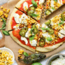 Roasted corn and jalapeño pizza on a wooden board with melted cheese and cilantro