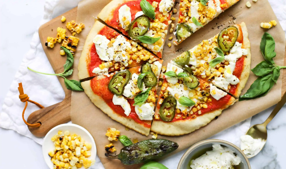 Roasted corn and jalapeño pizza on a wooden board with melted cheese and cilantro