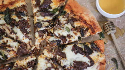Short Rib Gorgonzola Pizza topped with caramelized onions and parsley on a wooden board.
