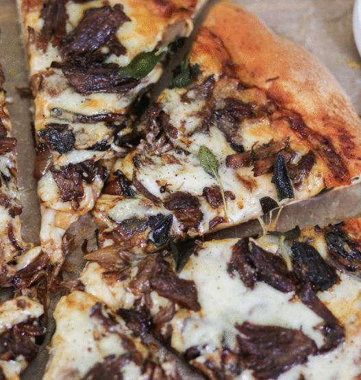 Short Rib Gorgonzola Pizza topped with caramelized onions and parsley on a wooden board.