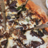 Short Rib Gorgonzola Pizza topped with caramelized onions and parsley on a wooden board.