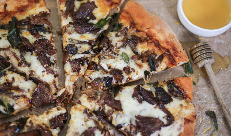 Short Rib Gorgonzola Pizza topped with caramelized onions and parsley on a wooden board.
