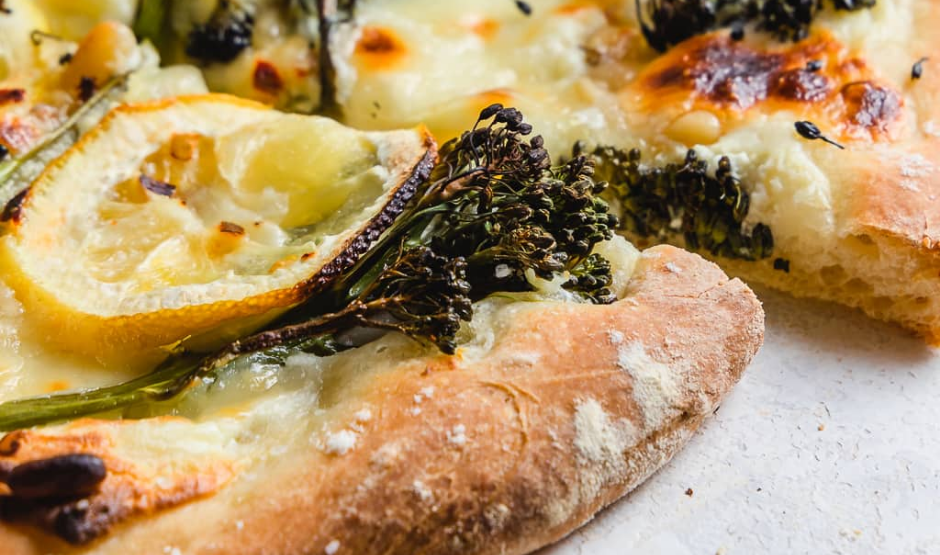 Charred broccolini lemon zest pizza topped with melted mozzarella and fresh basil