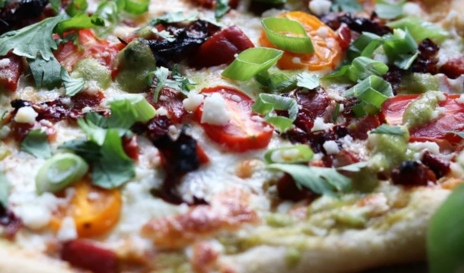 Close-up of Hatch Chile & Oaxaca Cheese Pizza with roasted green chiles, melted creamy cheese, caramelized onions, and fresh cilantro on a golden crust