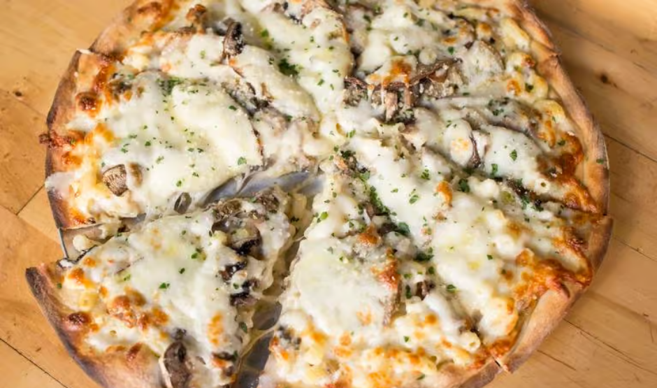 Overhead shot of golden-baked Truffle Mac and Cheese Pizza with bubbling cheese and truffle oil drizzle on a wooden board.