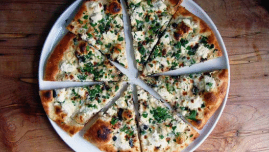 Ricotta garlic white pizza topped with mozzarella, roasted garlic, and parsley on a rustic wooden board