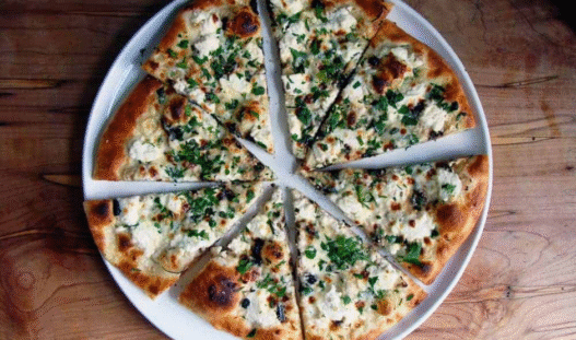 Ricotta garlic white pizza topped with mozzarella, roasted garlic, and parsley on a rustic wooden board