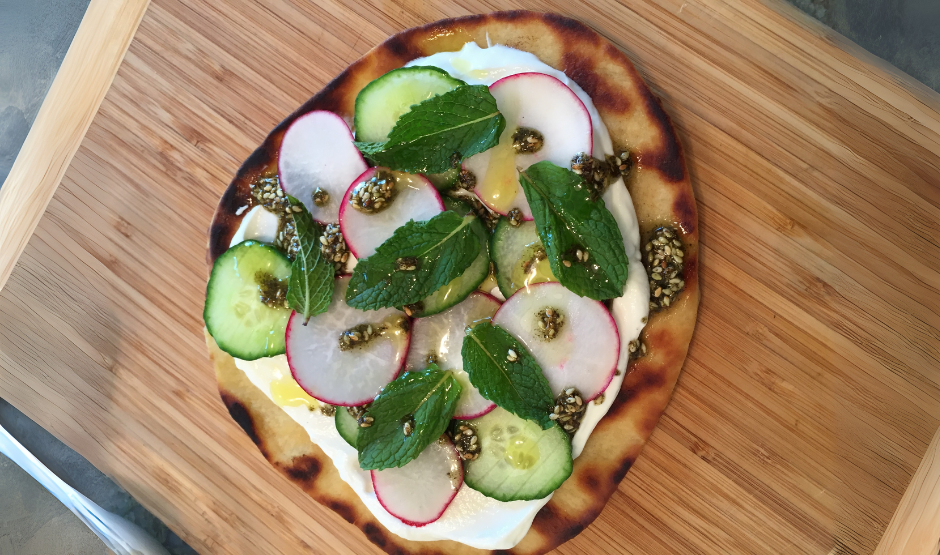 Zaatar & Labneh Flatbread Pizza topped with cherry tomatoes, herbs, and red onion on a white plate
