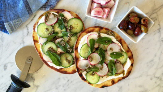 Zaatar & Labneh Flatbread Pizza topped with cherry tomatoes, herbs, and red onion on a white plate