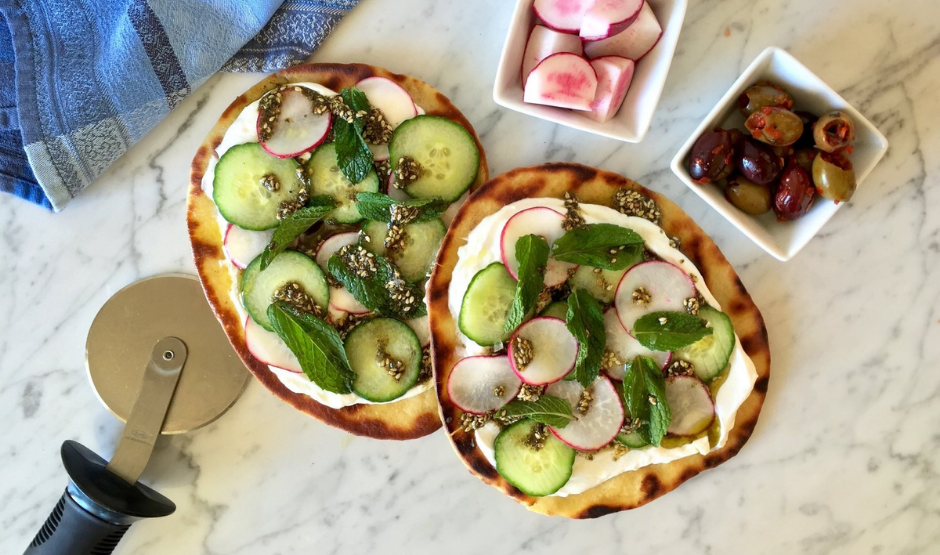 Zaatar & Labneh Flatbread Pizza topped with cherry tomatoes, herbs, and red onion on a white plate