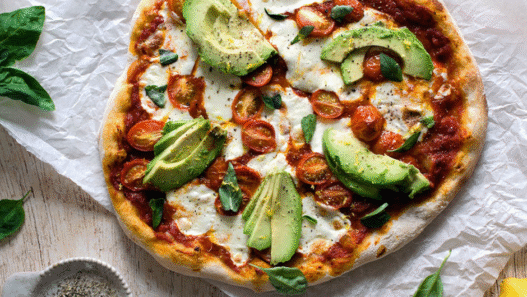 Avocado & Heirloom Tomato Pizza topped with arugula and basil on golden crust